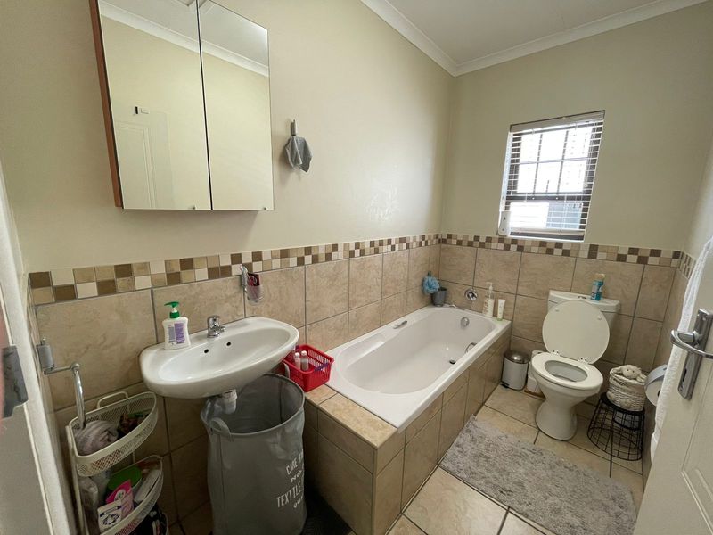 A functional bathroom featuring a built-in bathtub, pedestal basin, toilet, and a mirrored medicine cabinet with neutral wall and floor tiling.