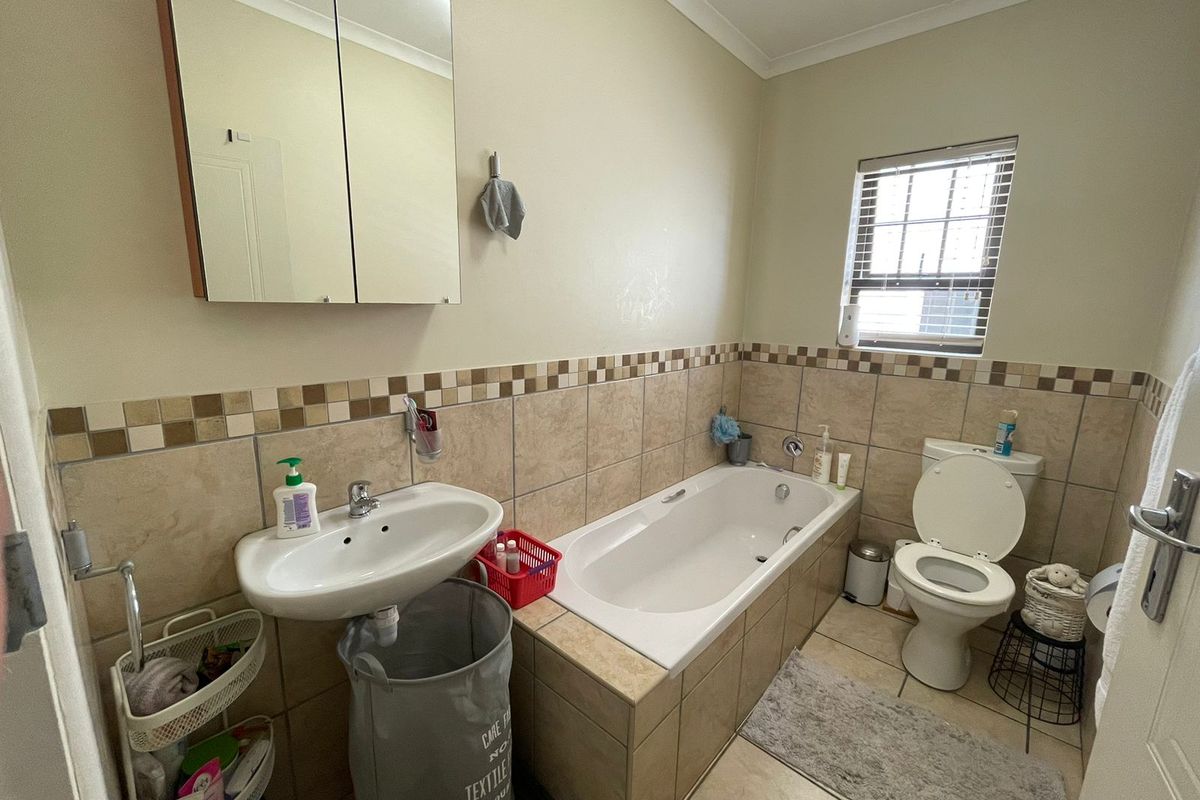 A functional bathroom featuring a built-in bathtub, pedestal basin, toilet, and a mirrored medicine cabinet with neutral wall and floor tiling.