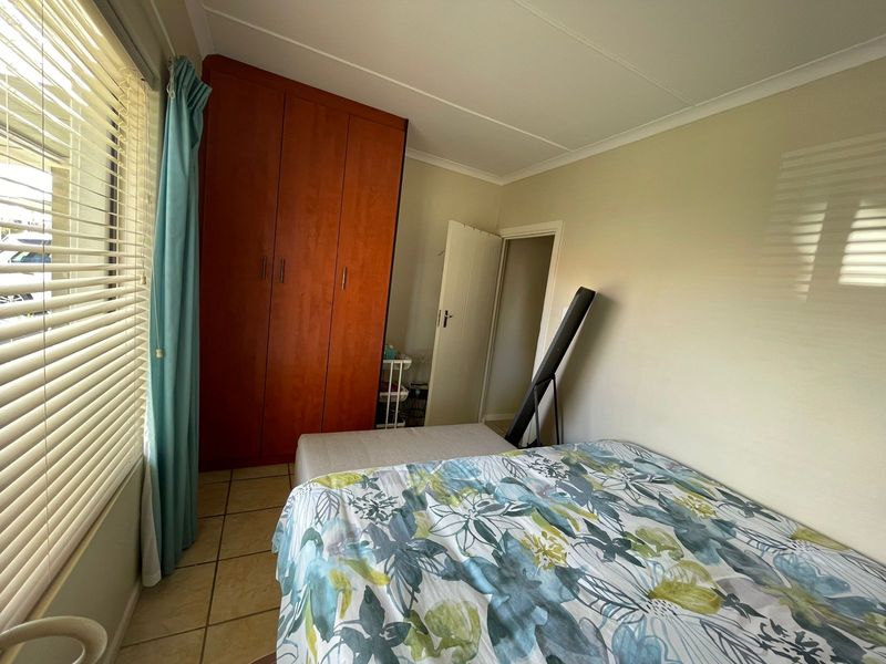 A functional bedroom featuring tiled flooring, a built-in wooden wardrobe, and venetian blinds, offering a practical space with neutral wall finishes.