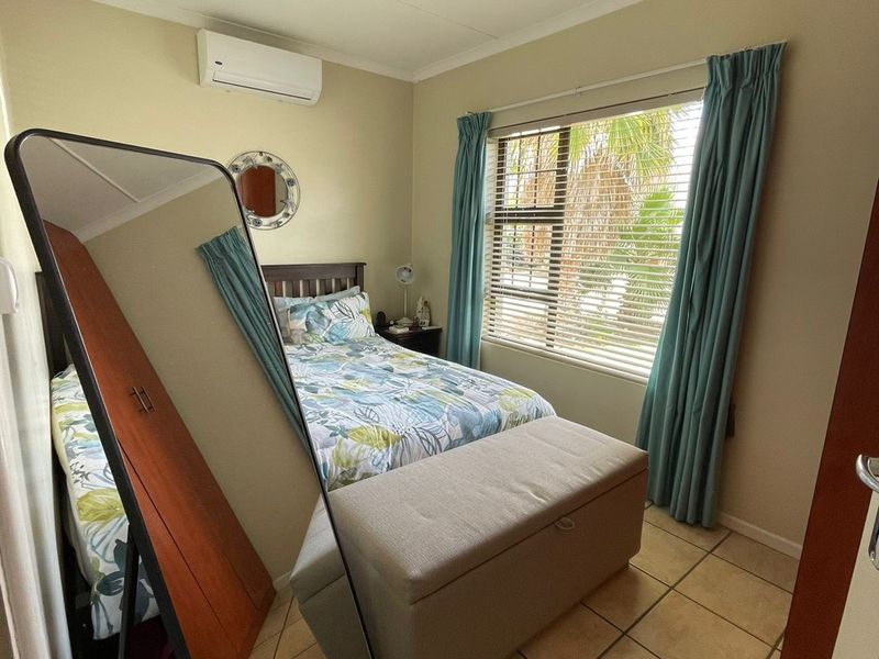 A compact bedroom featuring tiled flooring, an air conditioning unit, and a window with blinds, offering a functional and comfortable living space.