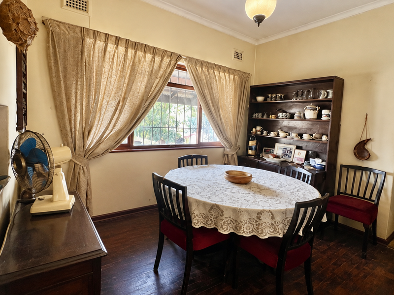 A traditional dining room featuring hardwood flooring, an arched entryway, and a window with curtains, offering a classic and functional space.