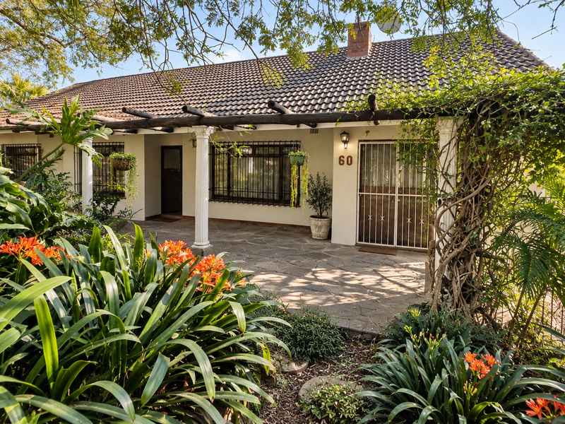 Front facade of a house featuring a stone-paved patio, timber pergola, and established garden surroundings.