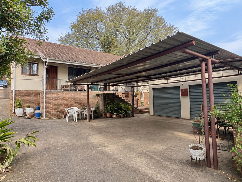 Front view of the property featuring a double garage, a large covered carport, and a paved driveway with an external staircase leading to the entrance.