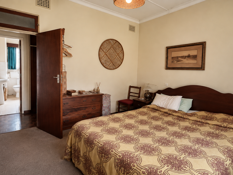 A well-proportioned bedroom featuring built-in cupboards, neutral wall finishes, and carpeted flooring, with direct access to an adjoining bathroom.