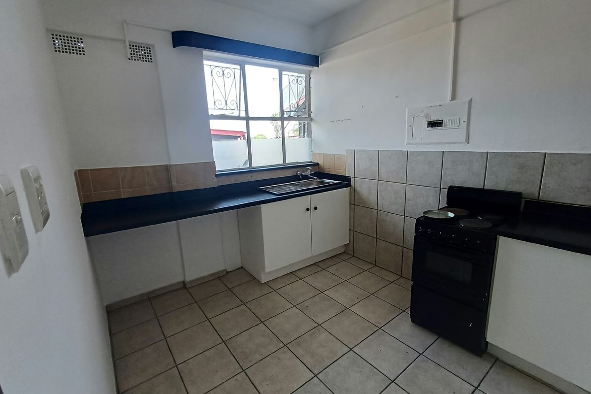 A functional kitchen featuring tiled flooring, a stainless steel sink, built-in cabinetry, and a freestanding stove, offering a blank canvas for modern updates.