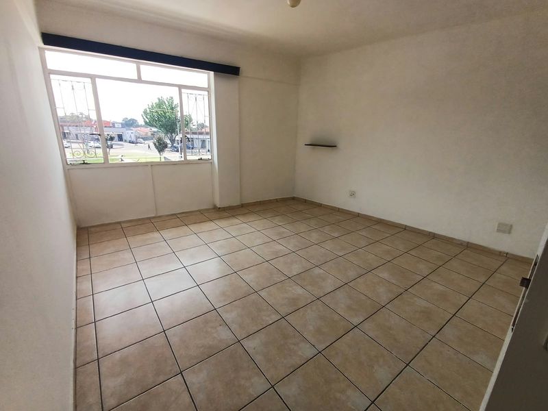 A bright, empty bedroom featuring neutral tiled flooring, large windows with security bars, and a clean, minimalist aesthetic ready for personalization.