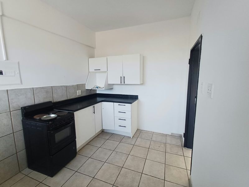 A functional kitchen featuring white cabinetry, black countertops, tiled backsplash, and tiled flooring, providing a clean and practical space for culinary activities.