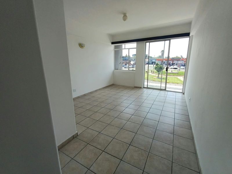 An empty, sunlit living area featuring neutral tiled flooring, a large window, and a sliding glass door providing access to the exterior.