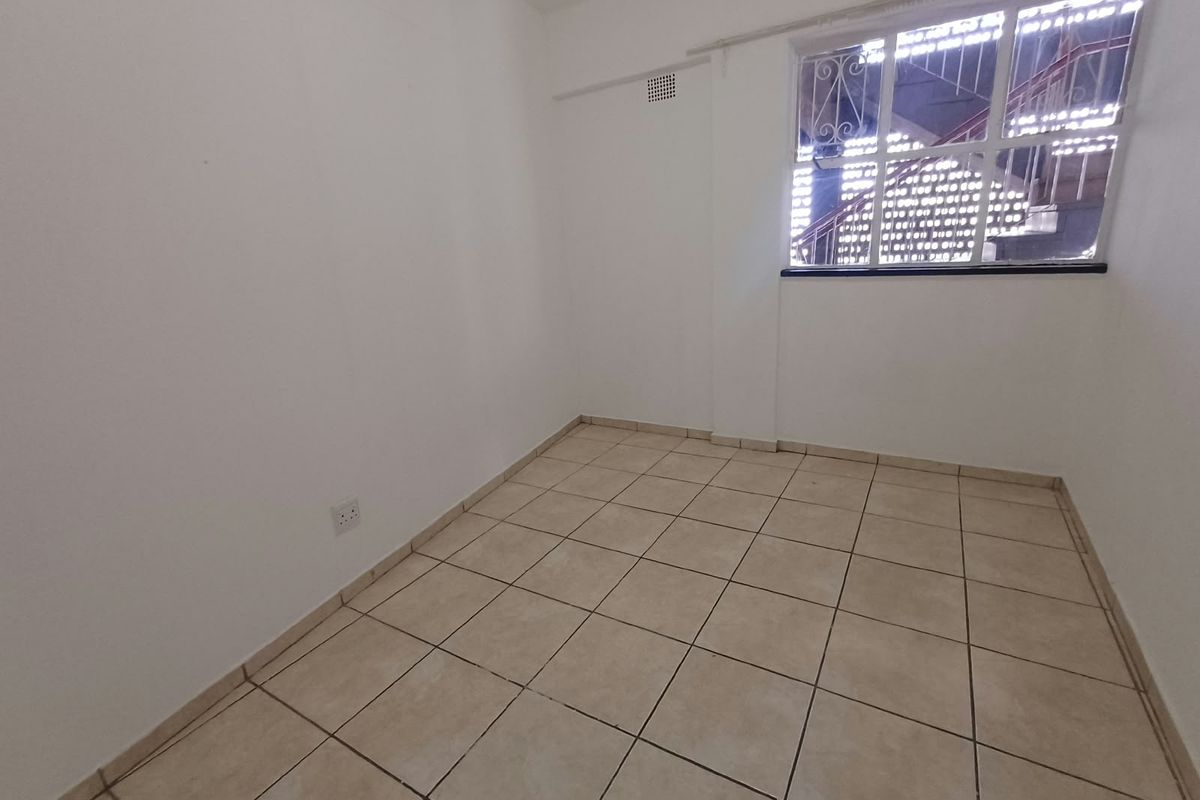 An empty bedroom featuring neutral tiled flooring, white walls, and a window fitted with security bars.