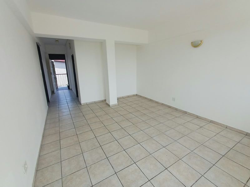 An empty, open-plan living area featuring neutral ceramic floor tiles, a structural support column, and a wall-mounted light fixture.
