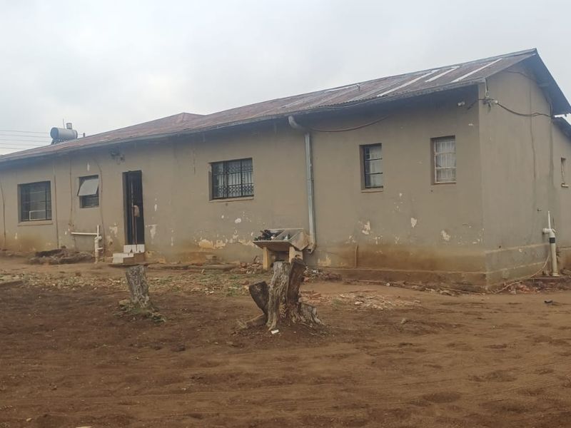 Rear view of a single-story house featuring a corrugated metal roof, solar water heater, and exterior walls requiring maintenance and repainting.