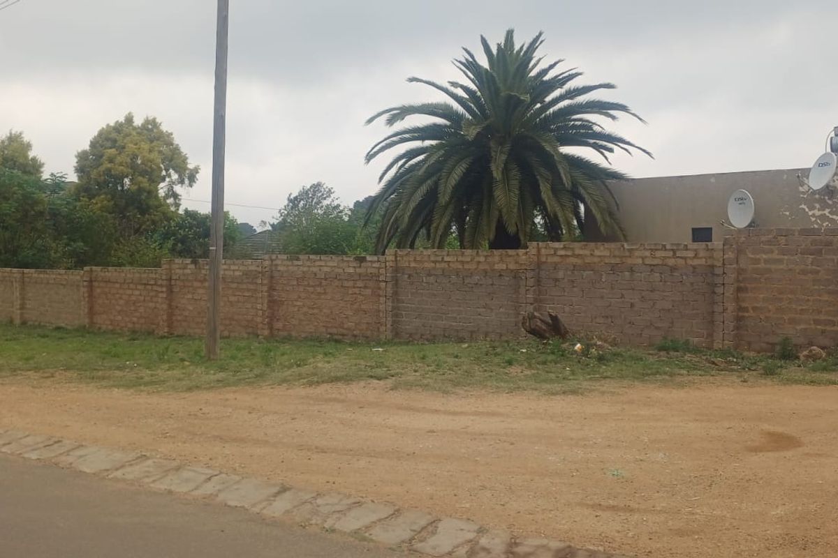 Street view of the property featuring a perimeter brick wall, metal gate, and exterior wall showing signs of wear.