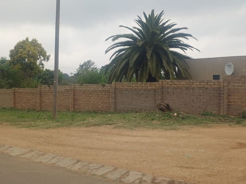 Street view of the property featuring a perimeter brick wall, metal gate, and exterior wall showing signs of wear.