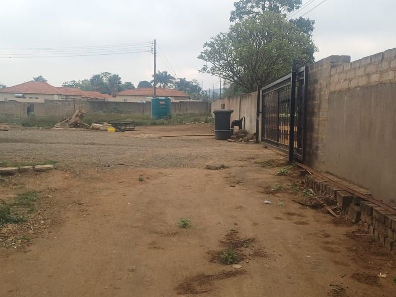 An unpaved driveway area featuring a perimeter wall and metal gate, showing signs of wear and unfinished exterior surfaces.