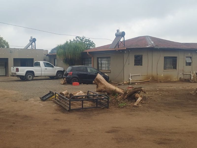 Rear view of a single-story house featuring solar water heating systems, metal security gates, and a large unpaved yard area.