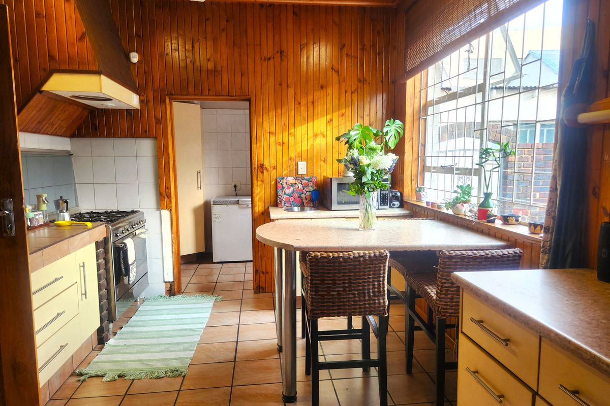 A functional kitchen featuring timber wall paneling, tiled floors, built-in cabinetry, and a gas stove, with an adjacent scullery area.
