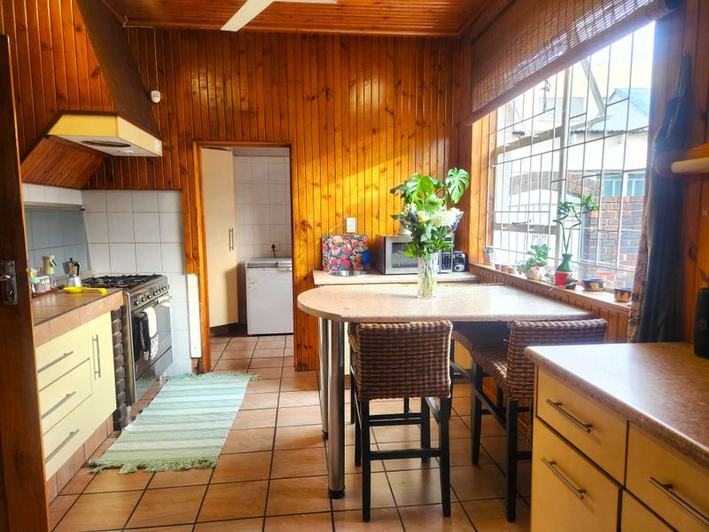 A functional kitchen featuring timber wall paneling, tiled floors, built-in cabinetry, and a gas stove, with an adjacent scullery area.