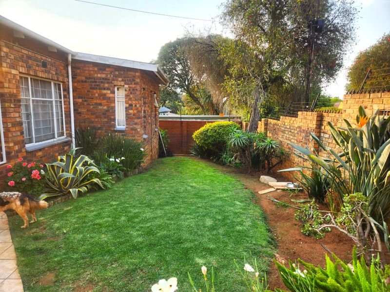 A private rear garden featuring a well-maintained lawn, established landscaping, and a brick boundary wall with security spikes.