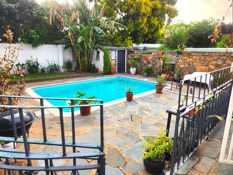 Outdoor pool area featuring stone paving, a swimming pool with ladder, and a stone boundary wall.