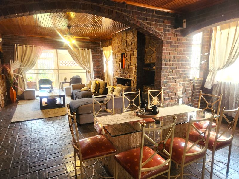 Spacious open-plan living and dining area featuring rustic exposed brick walls, a stone fireplace, and warm timber ceilings with tiled flooring.