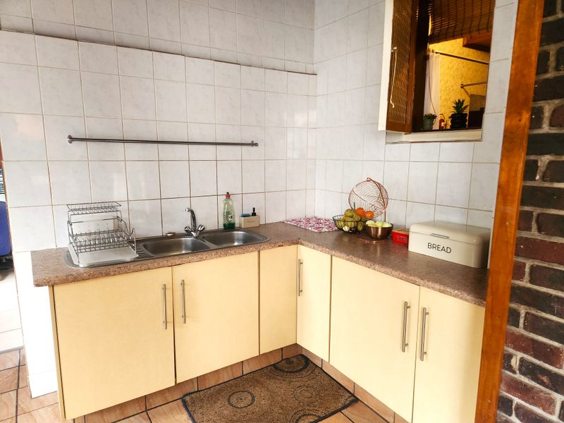 A functional kitchen corner featuring laminate countertops, a double stainless steel sink, and tiled splashbacks with built-in cabinetry.