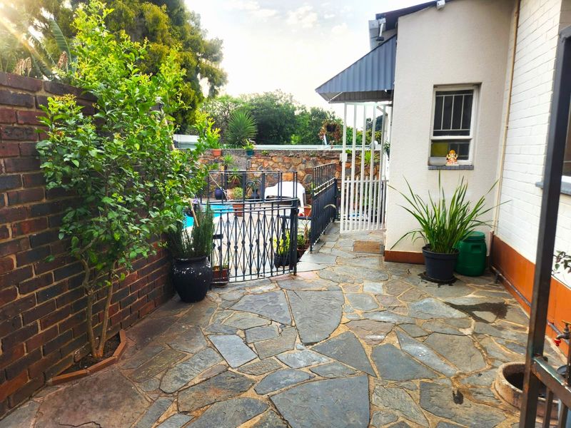 Rear exterior area featuring a stone-paved patio, brick boundary wall, and a gated swimming pool area with metal security fixtures.