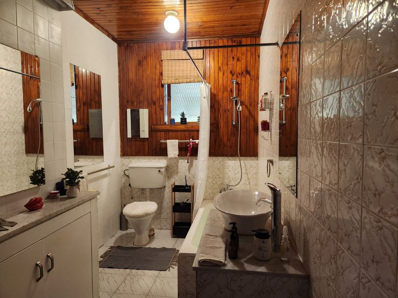 A functional bathroom featuring a vessel sink, vanity cabinet, bathtub with shower mixer, and distinctive timber wall and ceiling paneling.