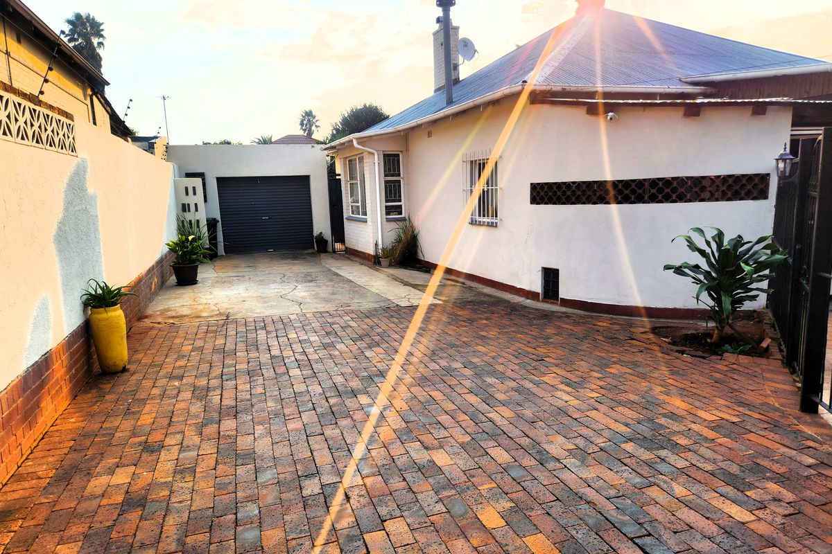 Rear exterior view featuring a brick paved driveway, single garage, and secure boundary walls with a metal roof structure.