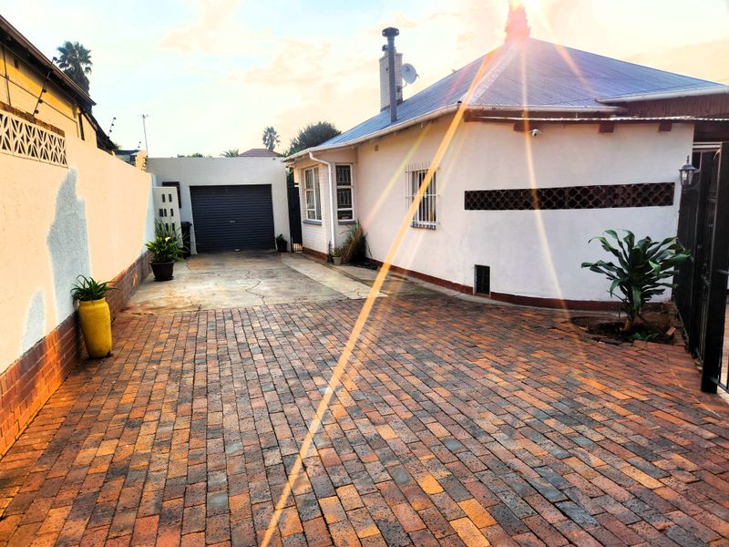 Rear exterior view featuring a brick paved driveway, single garage, and secure boundary walls with a metal roof structure.