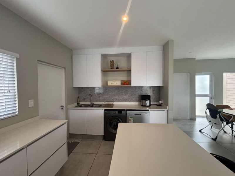 Modern kitchen featuring white cabinetry, stone countertops, integrated appliances, and tiled flooring, offering a clean and functional workspace.