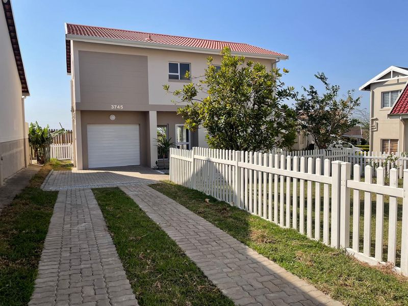 Front elevation of a two-story residential house featuring a paved driveway, white picket fence, and a single garage.