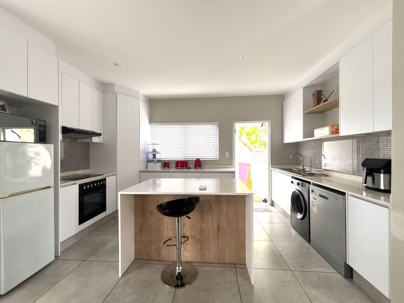 Modern kitchen featuring white cabinetry, stone countertops, a central island, and integrated appliances with tiled flooring and direct access to the exterior.