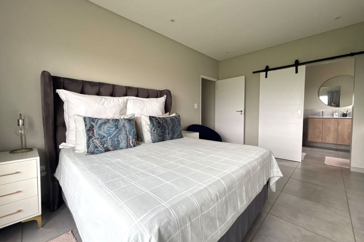 A modern bedroom featuring neutral wall tones, large format floor tiles, and a sliding barn door providing access to an en-suite bathroom.