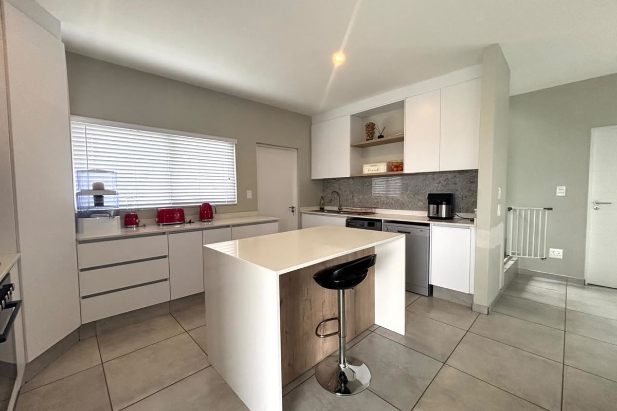 Modern kitchen featuring white cabinetry, stone countertops, a central island, and tiled flooring, offering a clean and functional workspace.