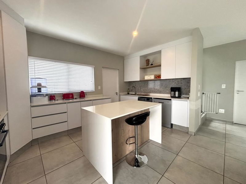 Modern kitchen featuring white cabinetry, stone countertops, a central island, and tiled flooring, offering a clean and functional workspace.