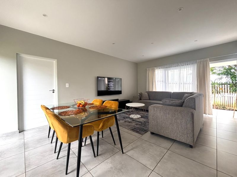 A bright open-plan living and dining area featuring neutral tiled flooring, recessed lighting, and direct access to an outdoor patio through a sliding glass door.