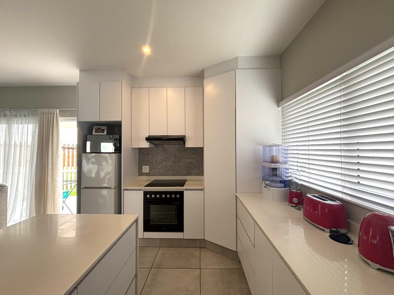 Modern kitchen featuring white cabinetry, stone countertops, built-in oven, electric cooktop, and tiled flooring with natural light from the adjacent patio area.