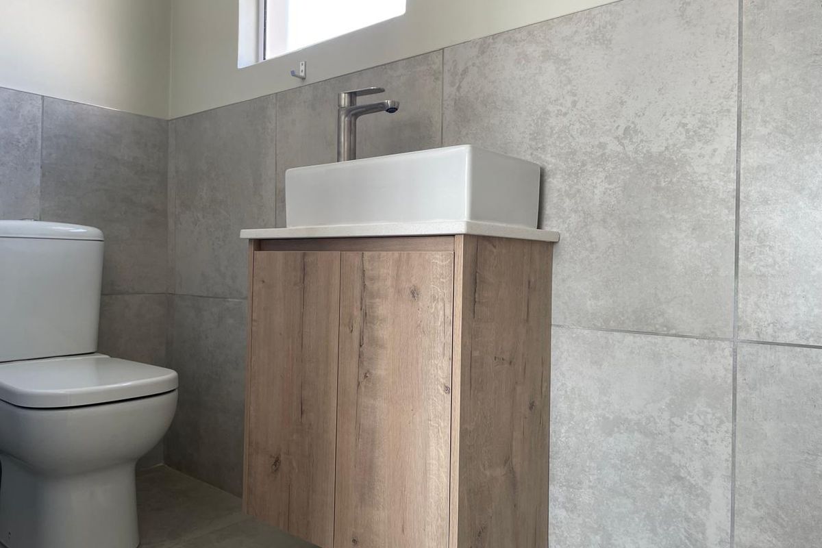 A modern bathroom featuring a wall-mounted wood-finish vanity with a vessel sink and a clean, tiled wall finish.