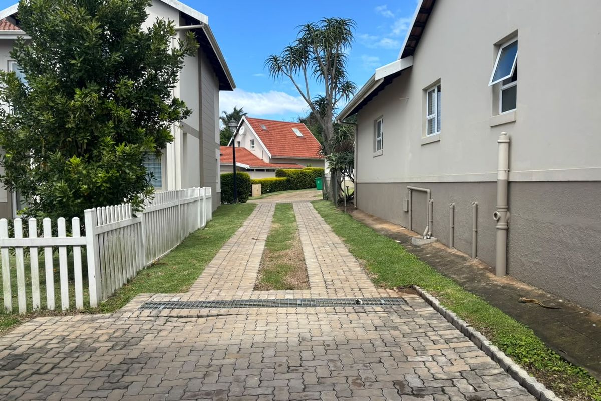 A paved driveway between two residential buildings featuring a white picket fence and integrated drainage system.