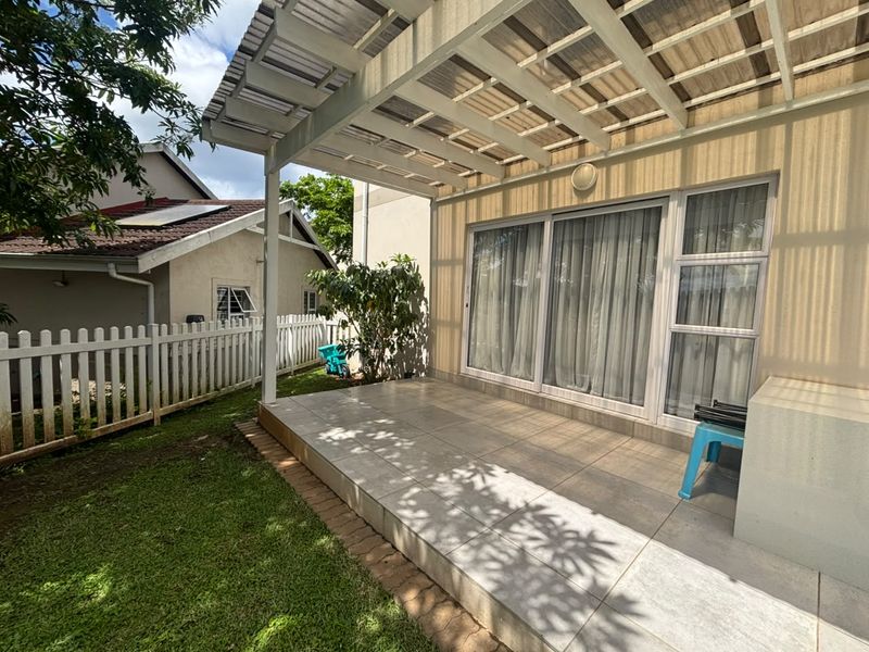 A covered patio area featuring tiled flooring, a translucent roof structure, and sliding glass doors providing access to the interior.