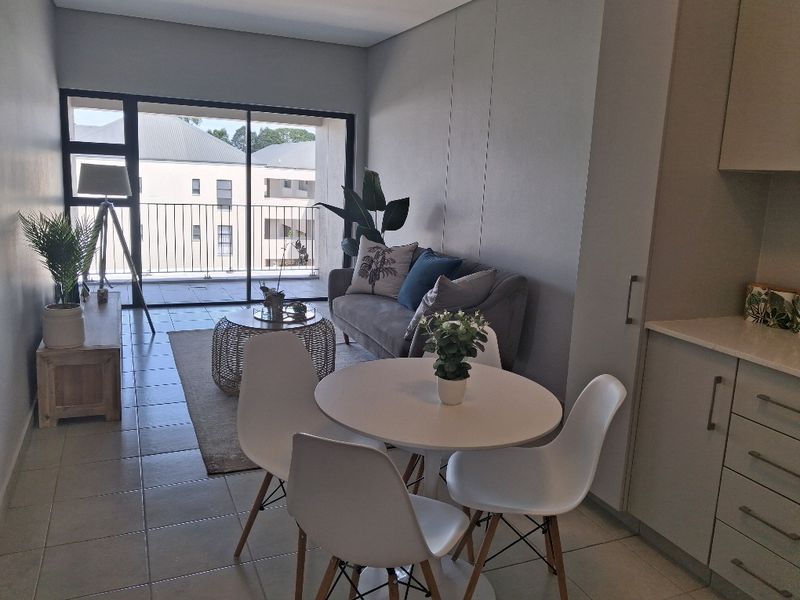 Modern open-plan living area featuring tiled floors, integrated kitchen cabinetry with stone countertops, and large sliding doors leading to a private balcony.