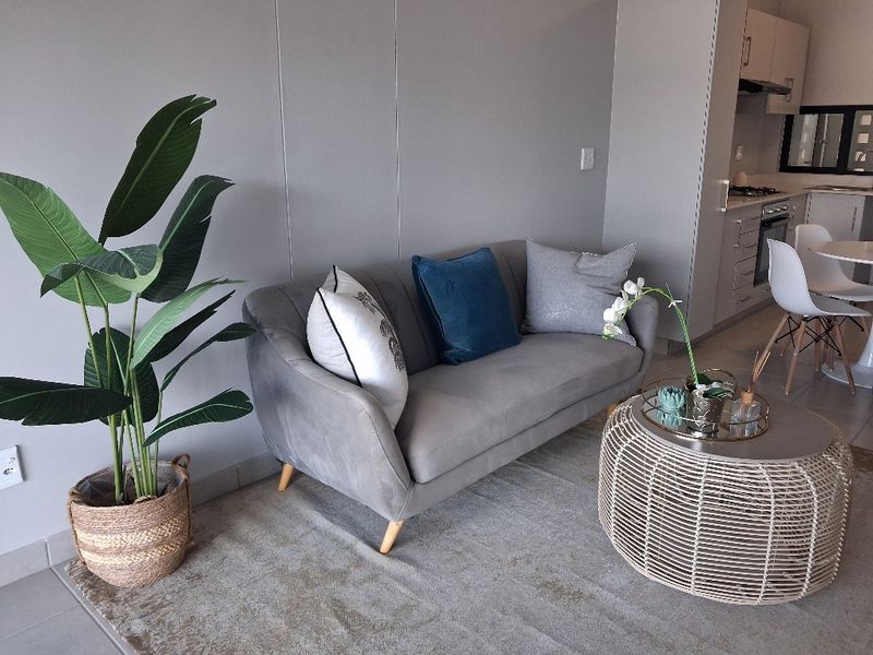 Modern open-plan living area featuring a sleek kitchen with built-in appliances and neutral tiled flooring, creating a cohesive and functional living space.