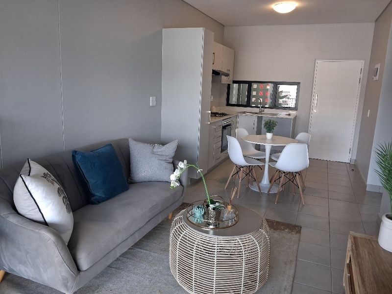 Modern open-plan living area featuring a compact kitchen with built-in cabinetry, oven, and extractor fan, complemented by neutral tiled flooring throughout.