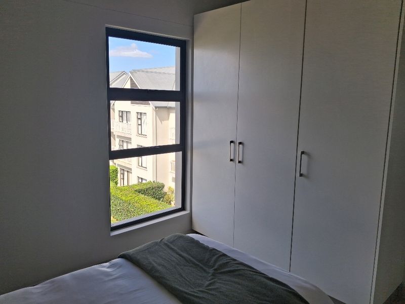 A bright bedroom featuring modern built-in cupboards and a large window with views of the surrounding complex.