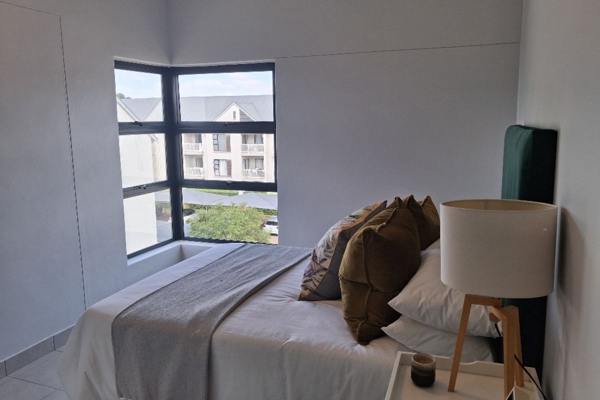 A well-lit bedroom featuring a modern corner window that provides natural light and views of the surrounding complex.