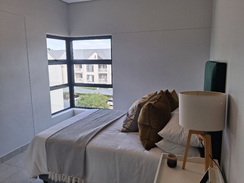 A well-lit bedroom featuring a modern corner window that provides natural light and views of the surrounding complex.