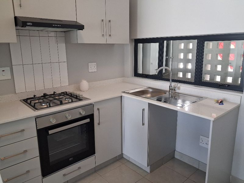 Modern kitchen featuring light grey cabinetry, quartz countertops, a gas hob, built-in oven, extractor fan, and a stainless steel sink.