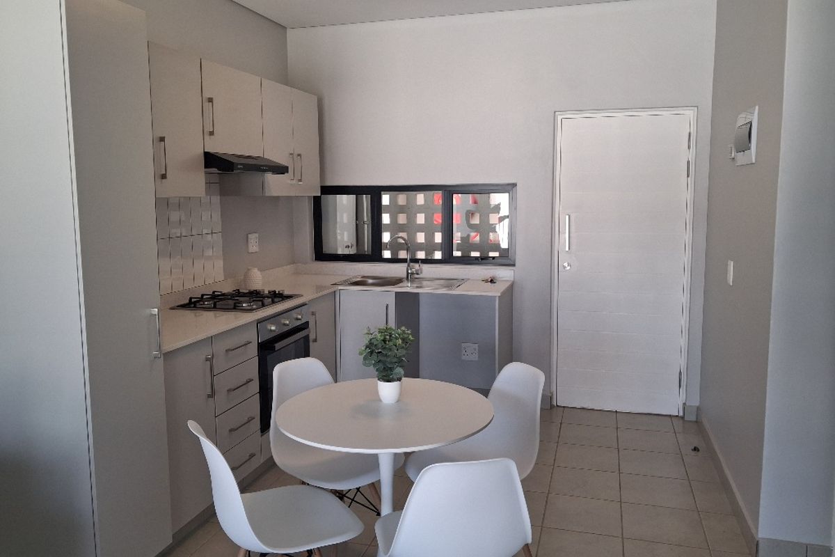 A modern, compact kitchen featuring built-in cabinetry, a gas hob, an electric oven, and a stainless steel sink with tiled flooring.