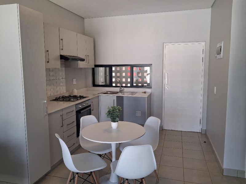 A modern, compact kitchen featuring built-in cabinetry, a gas hob, an electric oven, and a stainless steel sink with tiled flooring.
