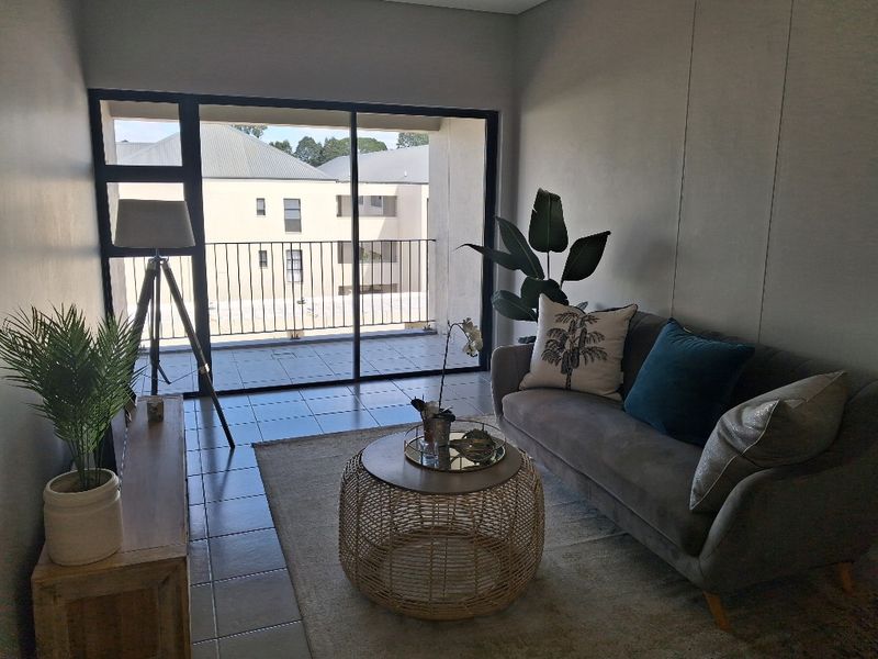 A well-lit living room featuring tiled flooring and large sliding glass doors that provide direct access to an outdoor balcony area.